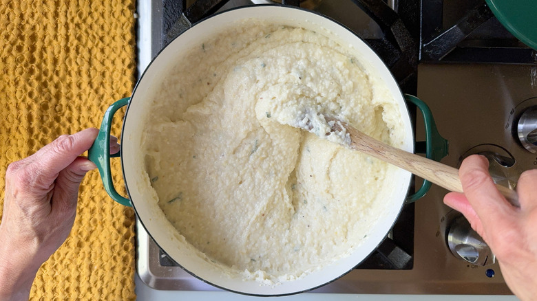 Stirring truffled grits with sage in pot on stovetop with wooden spoon