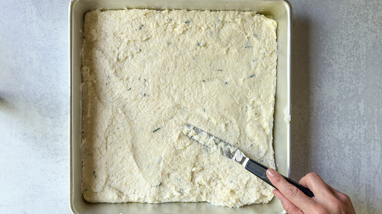 Cheesy truffled grits in square baking pan with offset spatula