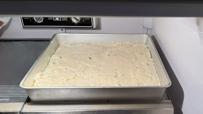 Cheesy truffled grits with sage in square baking pan in refrigerator