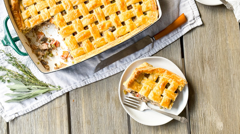 Chicken, mushroom, and winter squash pot pie in serving dish with cut piece on place and fresh herbs