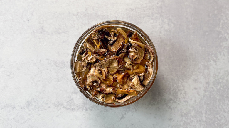 Mixed dried mushrooms soaking in water in glass bowl