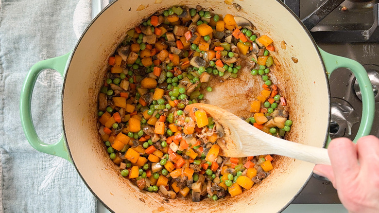 Stirring peas and mushrooms into cooked butternut squash and mirepoix with wooden spoon in Dutch oven on stovetop