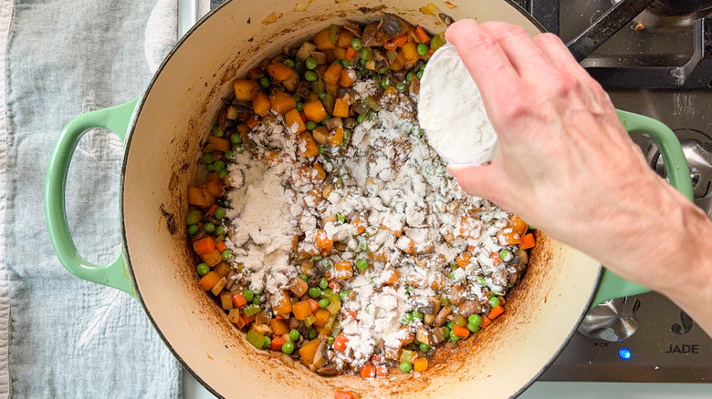 Sprinkling flour over cooked vegetables in Dutch oven on stovetop