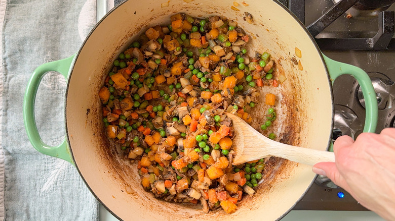 Stirring pot pie vegetables in Dutch oven on stovetop with wooden spoon