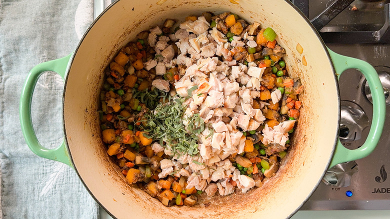 Cooked chicken, fresh herbs, and pot pie vegetables in Dutch oven on stovetop