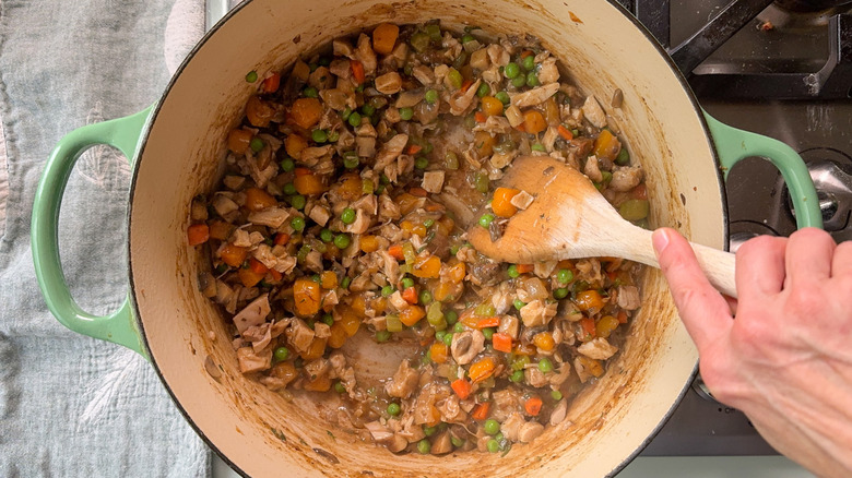 Stirring chicken broth into cooked pot pie chicken and vegetables in Dutch oven with wooden spoon