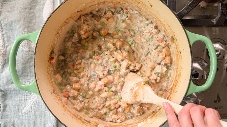 Stirring sour cream into chicken pot pie filling in Dutch oven with wooden spoon