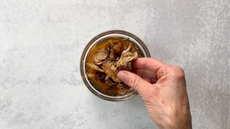 Lifting soaked mixed dried mushrooms from water in glass bowl with fingers