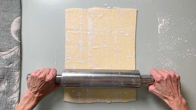 Rolling out puff pastry on work surface with rolling pin