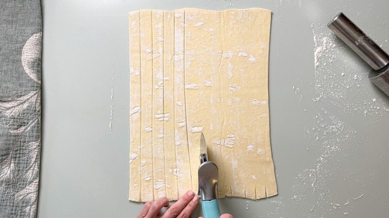 Cutting puff pastry dough with pizza cutter into strips