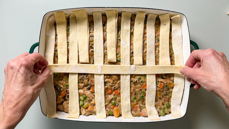 Making a lattice with puff pastry dough strips over pot pie filling in casserole dish