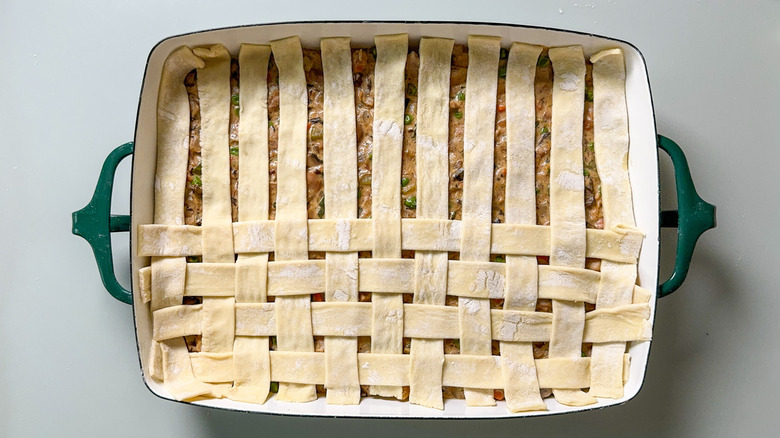 Half lattice of puff pastry strips over pot pie filling in casserole dish