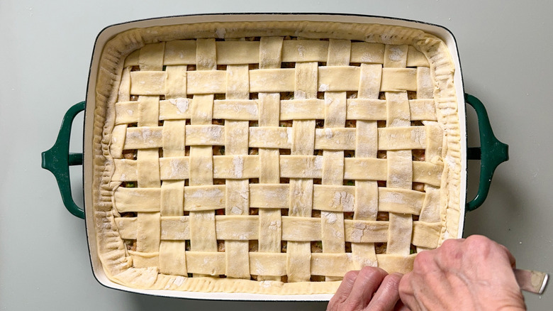 Crimping puff pastry dough lattice crust on top of pot pie in casserole dish