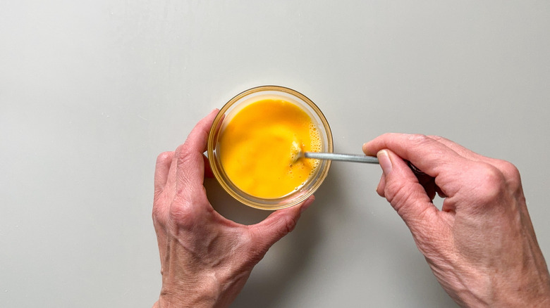 Whisking egg and water in a small glass bowl with a fork