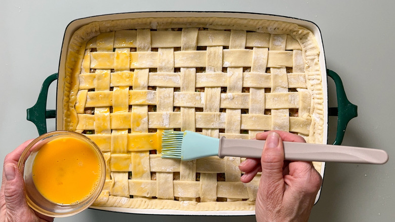 Brushing egg wash on puff pastry dough lattice crust on pot pie in casserole dish