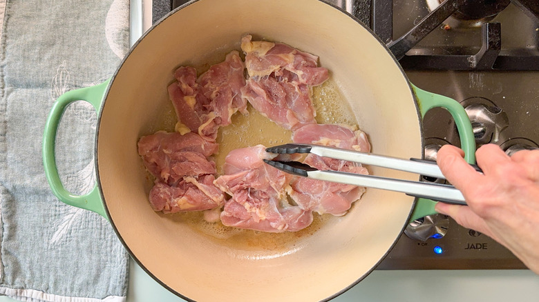 Chicken thighs cooking in butter in Dutch oven on stovetop with tongs