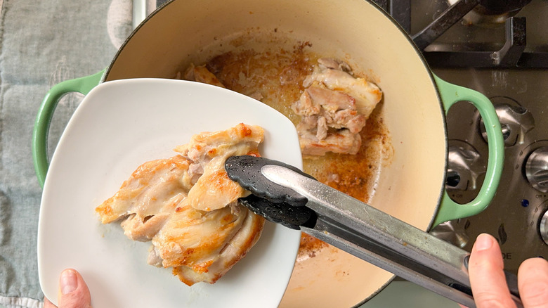 Removing browned chicken thighs from pot with tongs on plate