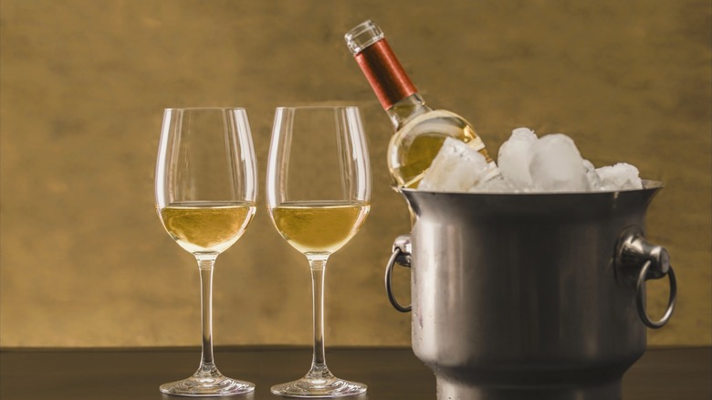 two glasses white wine next to wine in ice bucket