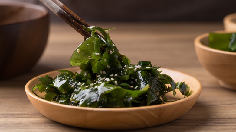 Wooden chopsticks gripping wakame seaweed salad