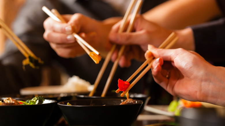 hands with four sets of chopsticks reaching into food bowls