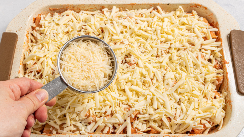Sprinkling cheese over a baking dish with more cheese on top