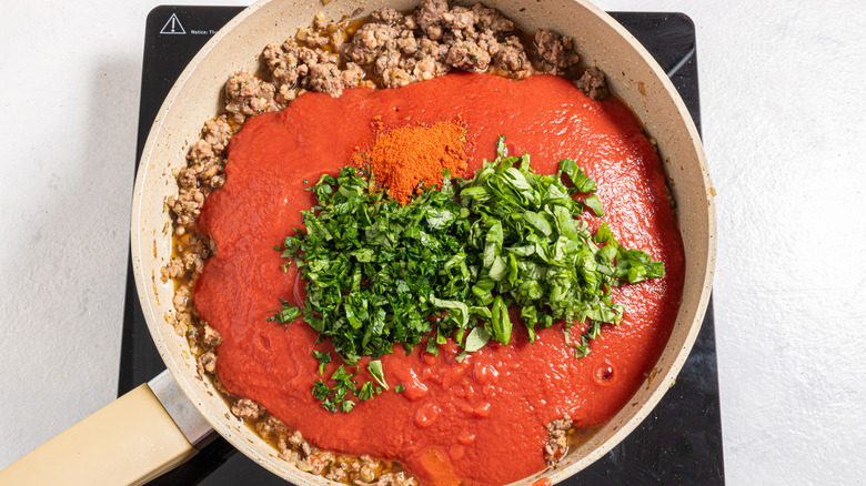 Skillet with ground meat, red sauce, and chopped herbs and spices
