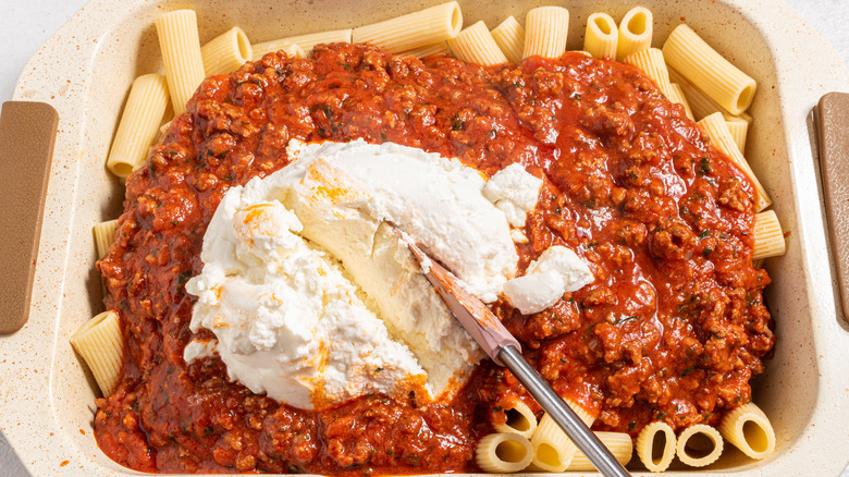 Baking dish with pasta, meat sauce, and ricotta cheese on top