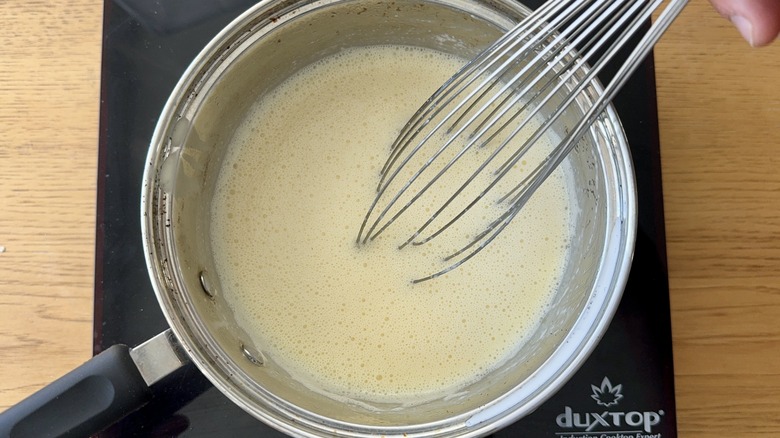 Milky mixture and whisk in saucepan