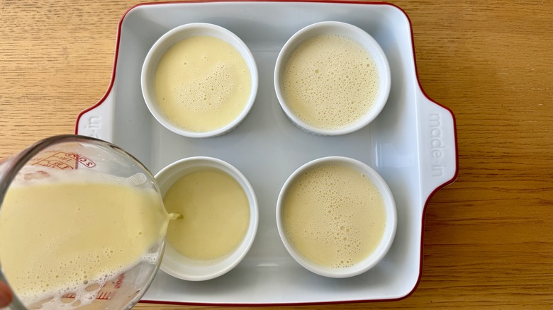 Milky liquid pouring into ramekins in baking dish