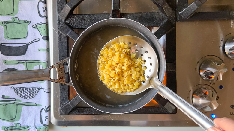 Ditalini pasta on slotted spoon over pot on stove