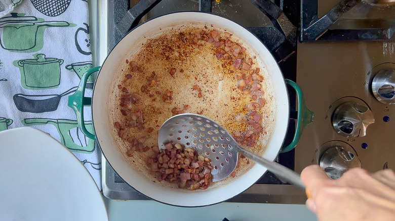 Removing crispy pancetta from pot with slotted spoon