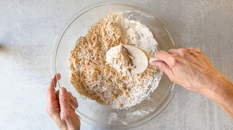 Mixing grated cheddar into dry ingredients for classic sausage balls with wooden spoon in glass bowl