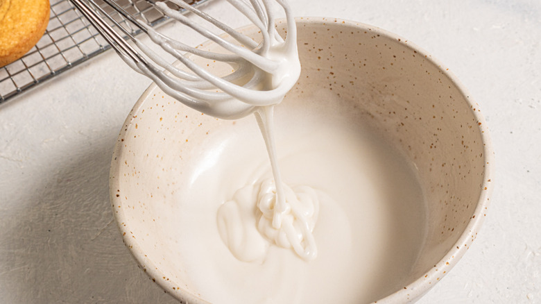 Whisk with sugar glaze dripping over a bowl
