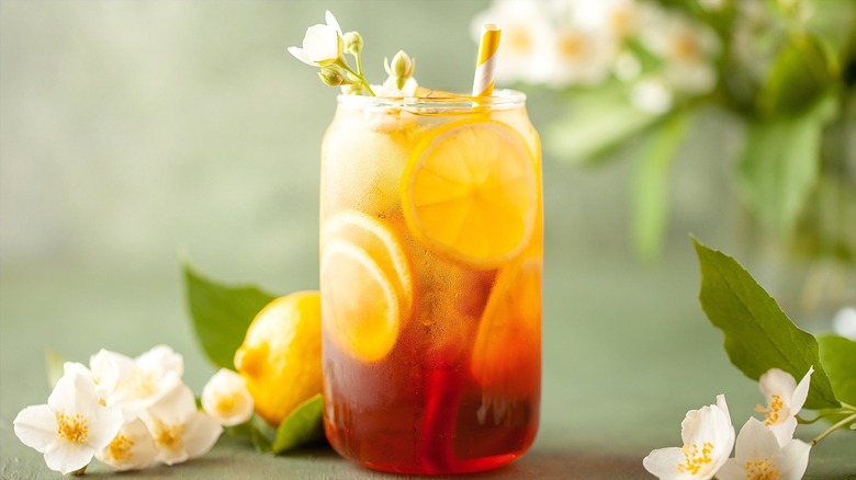 A glass of iced jasmine tea with lemon slices surrounded by jasmine flowers
