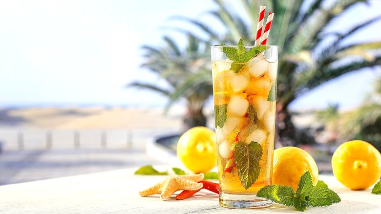 Glass of iced tea with mint leaves, lemon, and a red and white striped straw