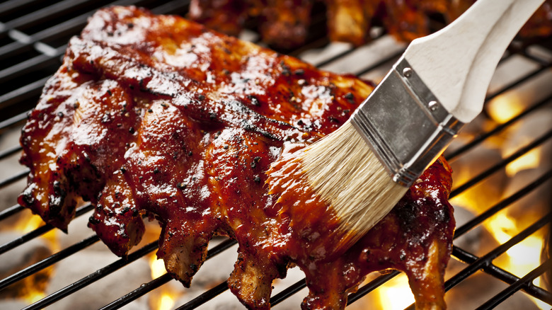 Ribs on a grill being slathered in barbecue sauce