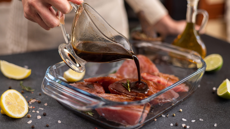 Person pours dark marinade into a glass pan of raw meat