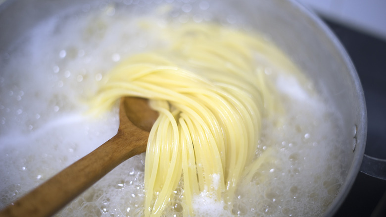 Wooden spoon stirring boiling pasta