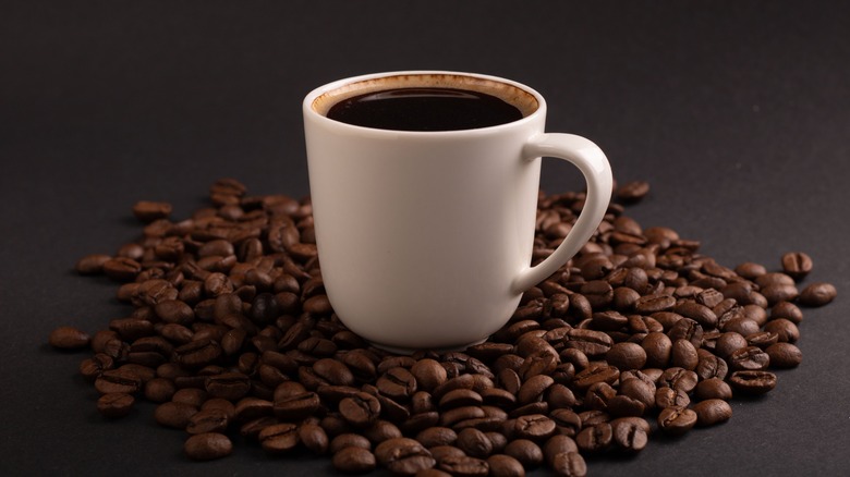 A cup of coffee surrounded by whole coffee beans