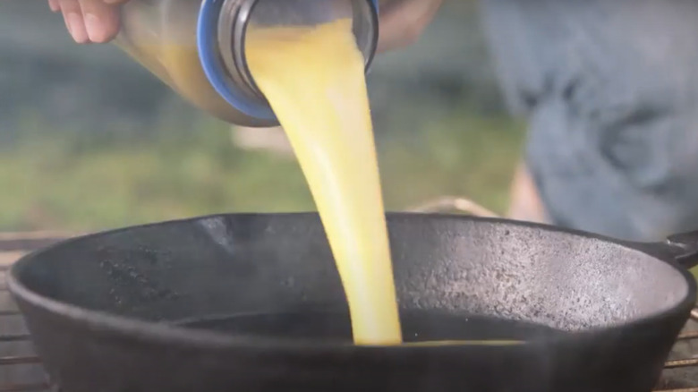 Pouring raw scrambled eggs into a skillet