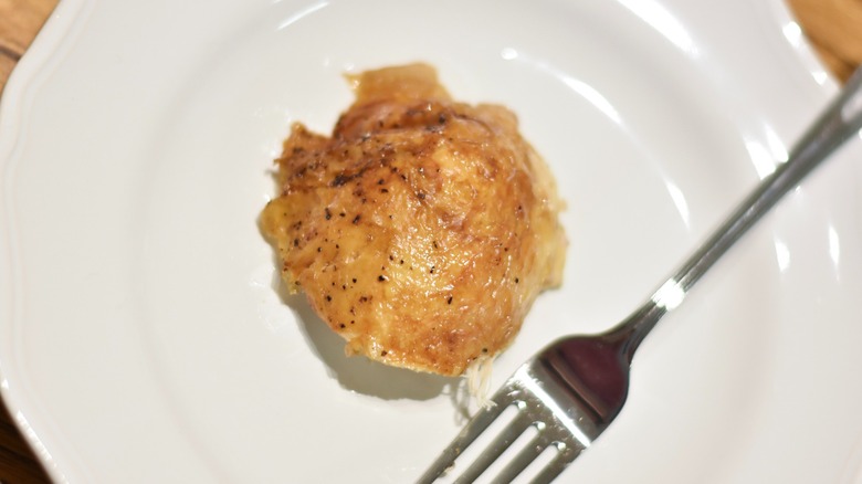 A piece of rotisserie chicken on a white plate with a fork