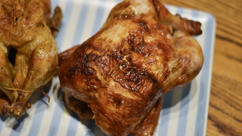 A Costco rotisserie chicken with crispy skin on a blue and white striped platter on a wooden table