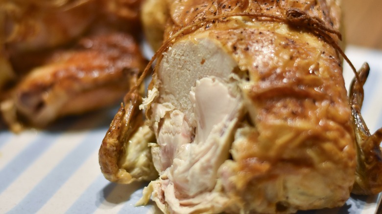 A rotisserie chicken tied with string cut on the breast on a blue and white striped platter