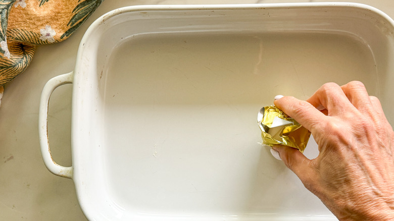 hand greasing baking dish with butter