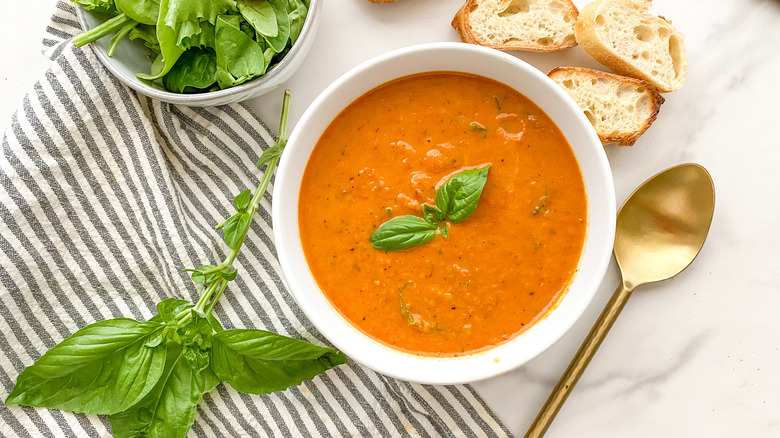 A bowl of tomato soup and  fresh basil
