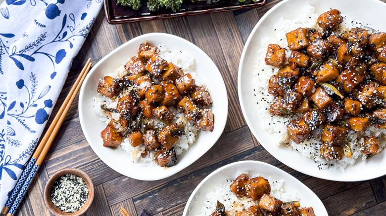 Crispy and sticky baked sesame tofu on rice on plates with chopstick