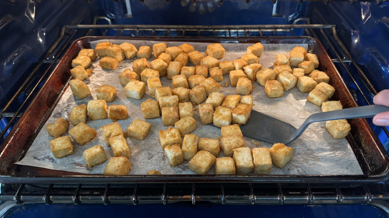 Flipping baked tofu cubes on parchment-lined baking sheet in oven