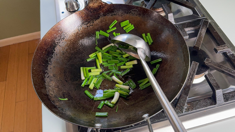 Stir-frying scallion pieces in hot oil in wok on stovetop