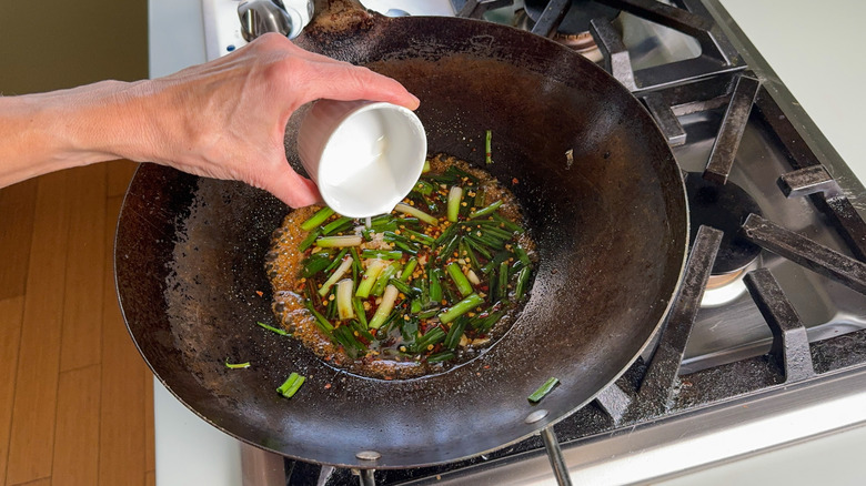 Adding cornstarch slurry to sesame sauce and scallions in wok on stovetop