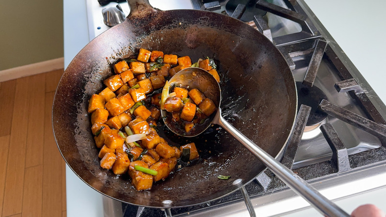 Stirring crispy and sticky baked sesame tofu in wok on stovetop